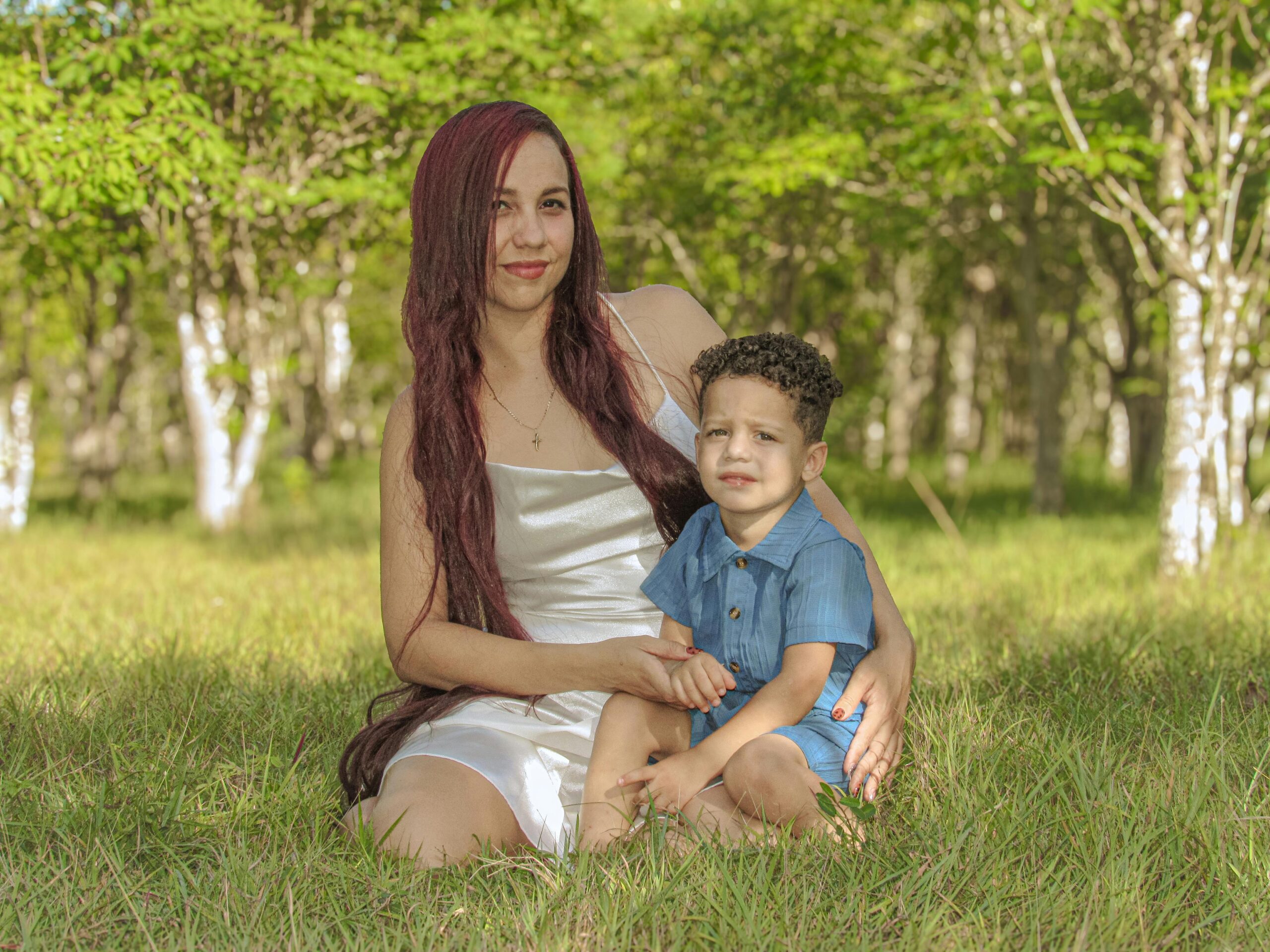 A mother and her child sitting on grass amidst vibrant green forest scenery.