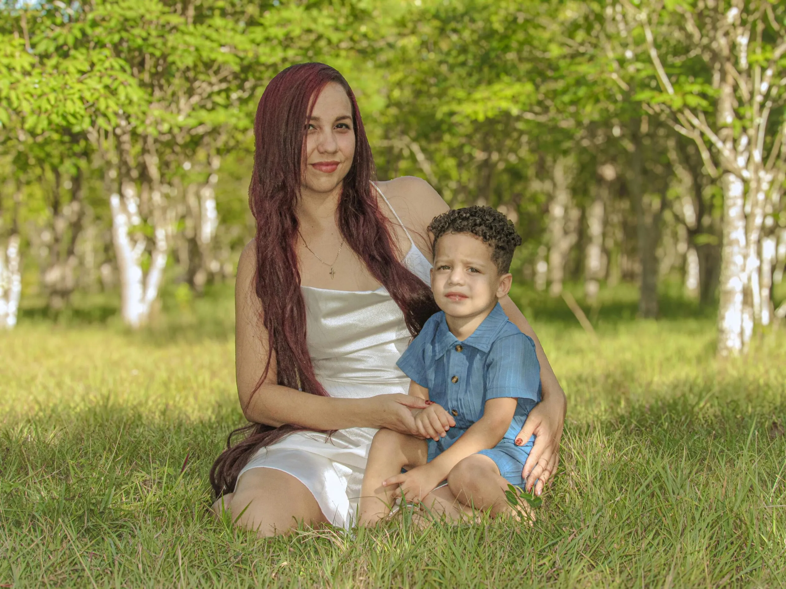 A mother and her child sitting on grass amidst vibrant green forest scenery.
