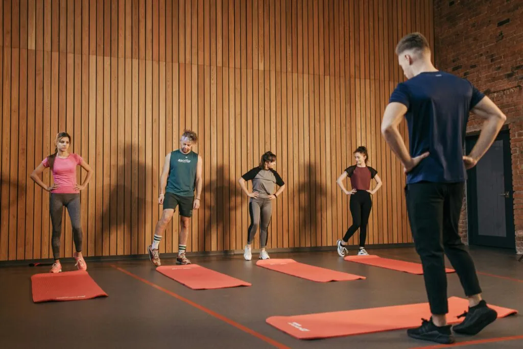 A group exercise class with a personal trainer leading stretching exercises in a gym.